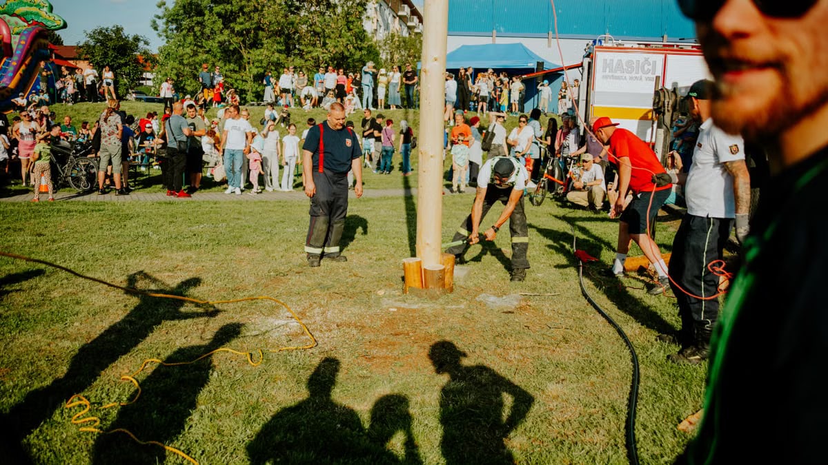 A vibrant summer festival with people gathered around a pole-raising event outdoors.